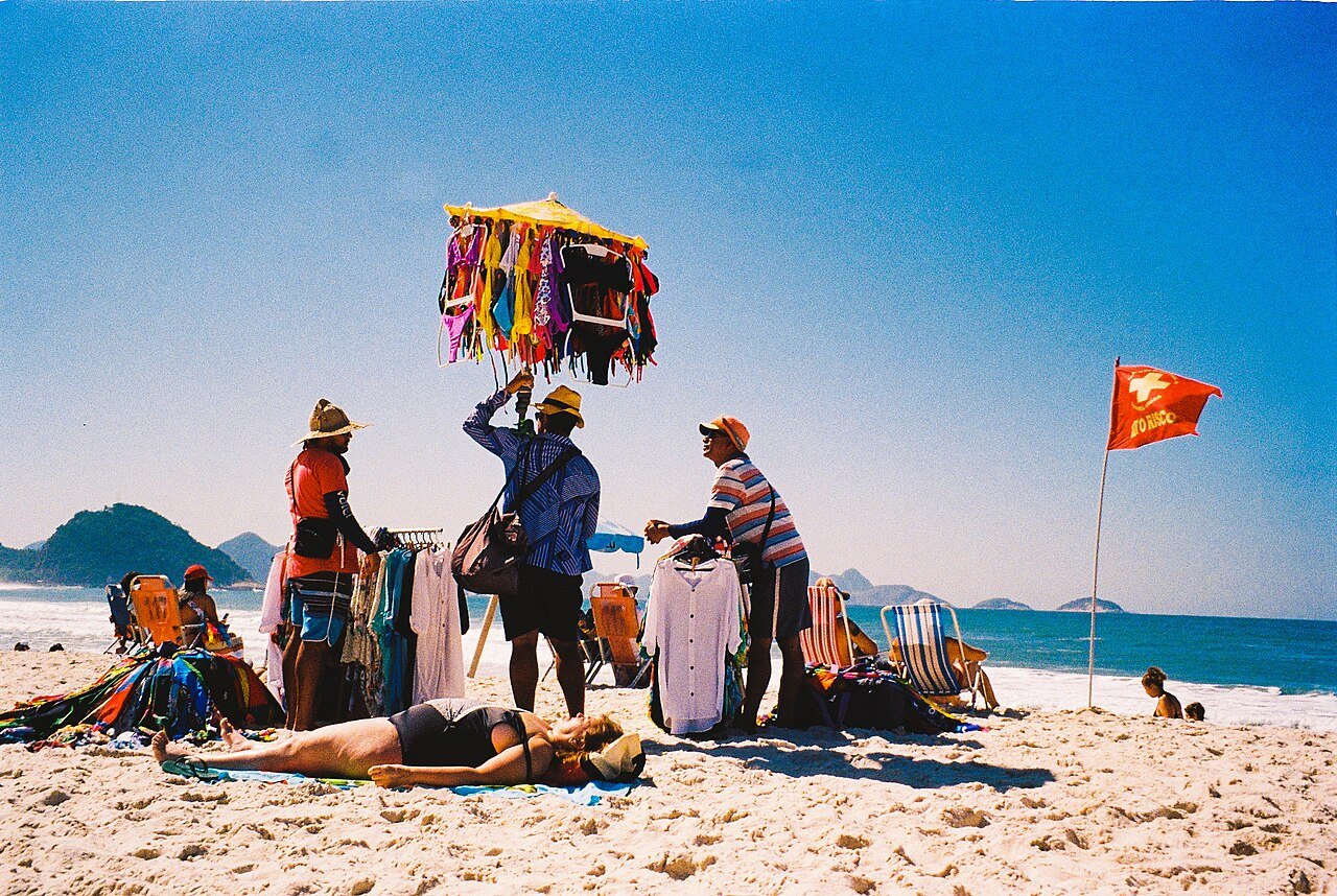 Ambulantes vendem roupas de praia em arara improvisada na areia, no Rio de Janeiro