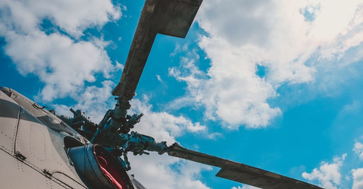 Rotor de helicóptero visto de baixo contra céu azul com nuvens