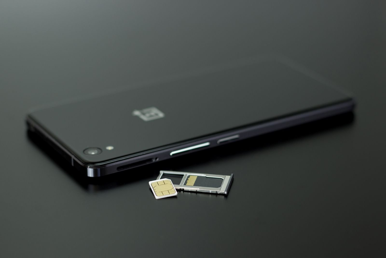 Smartphone preto ao lado de um chip SIM e da bandeja do cartão