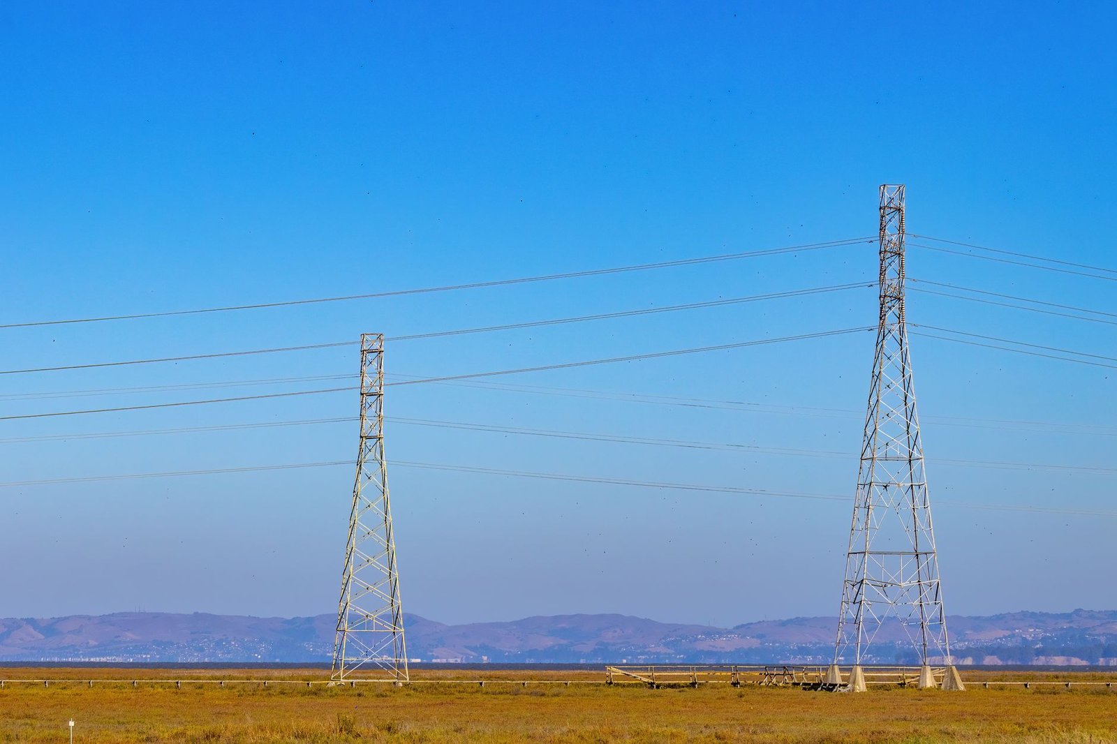 Duas torres de transmissão de energia com cabos de alta tensão sob céu azul; foto ilustrativa