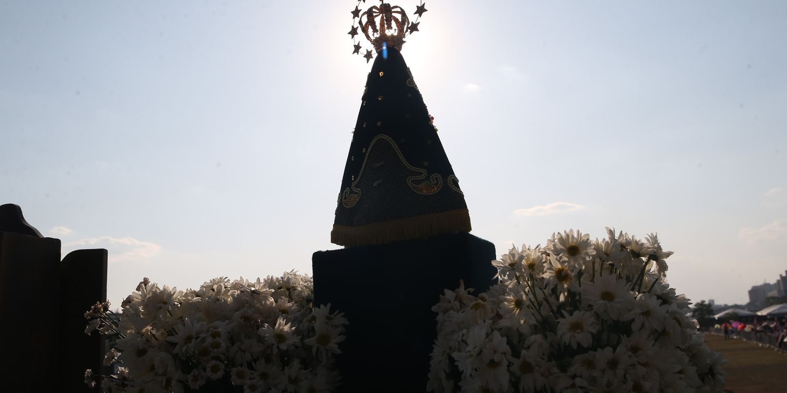 Imagem de Nossa Senhora Aparecida em contraluz, cercada de margaridas brancas
