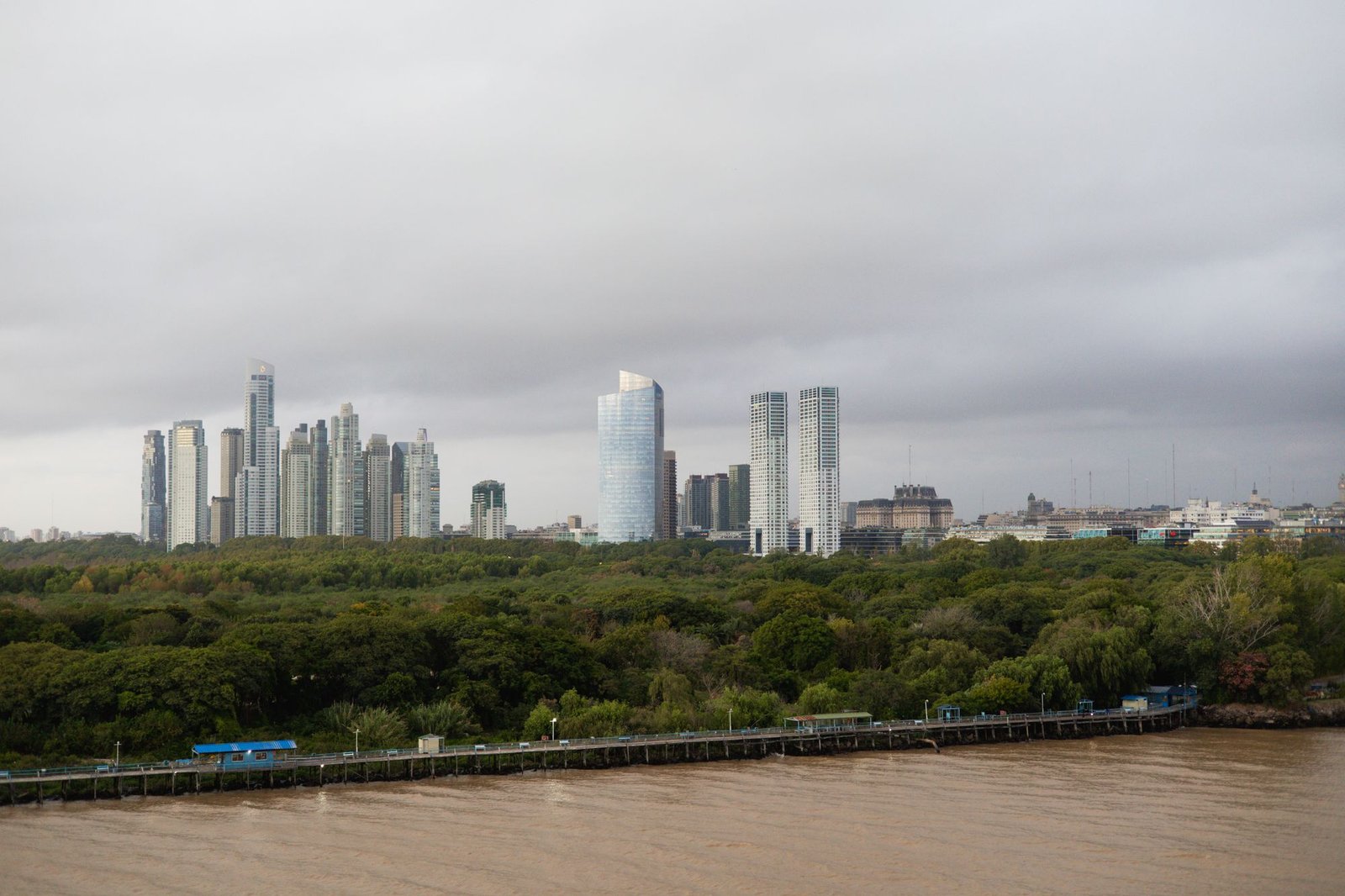Arranha-céus de Buenos Aires acima de área verde e do Rio da Prata sob céu nublado