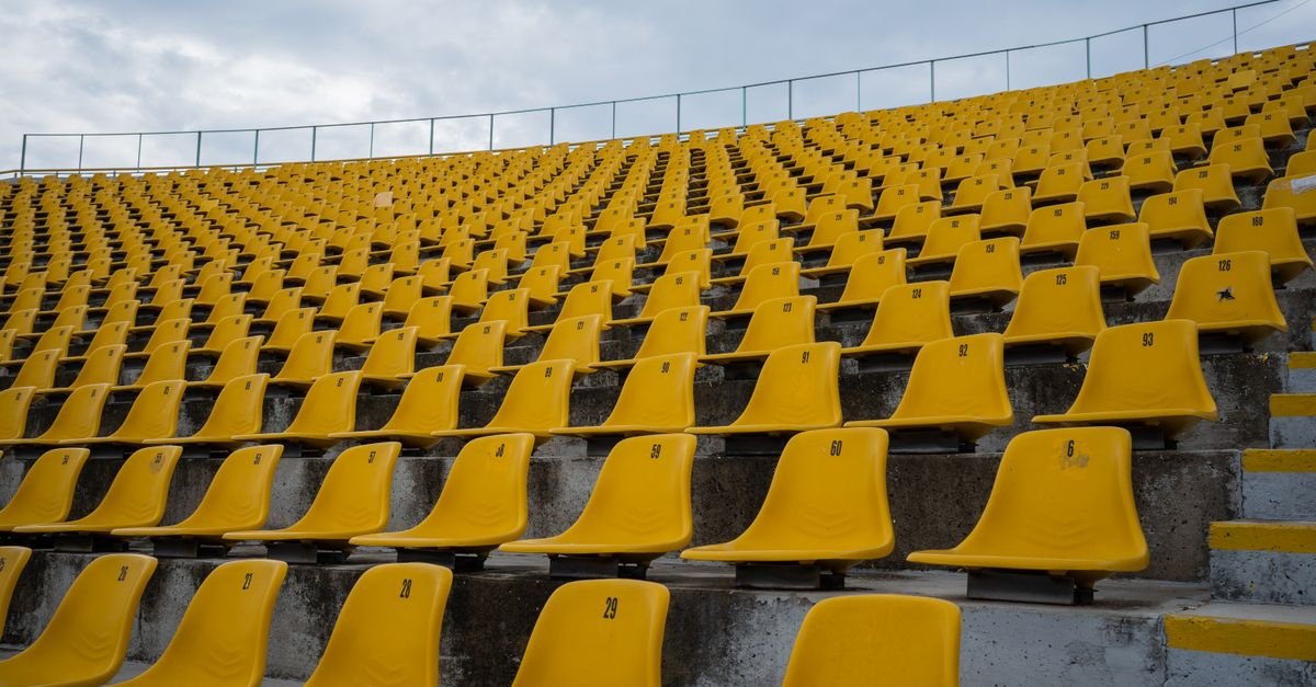 Fileiras de assentos amarelos vazios em arquibancada de estádio, com numeração nas cadeiras