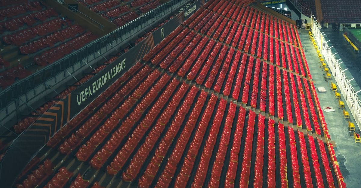 Arquibancada vazia de estádio com assentos vermelhos e placa da Uefa Europa League na divisória