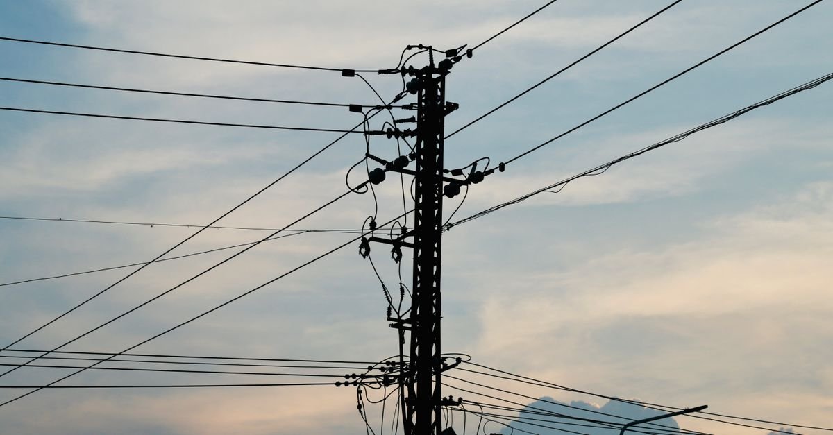 Silhueta de poste de distribuição de energia com fios contra o céu no fim da tarde