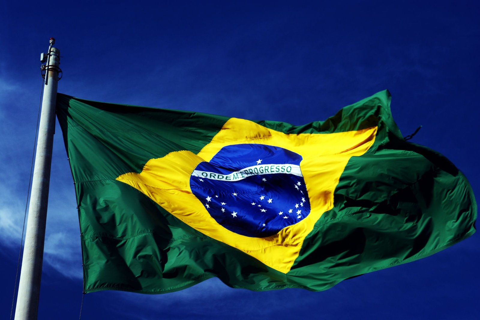 Bandeira do Brasil hasteada em mastro contra o céu azul