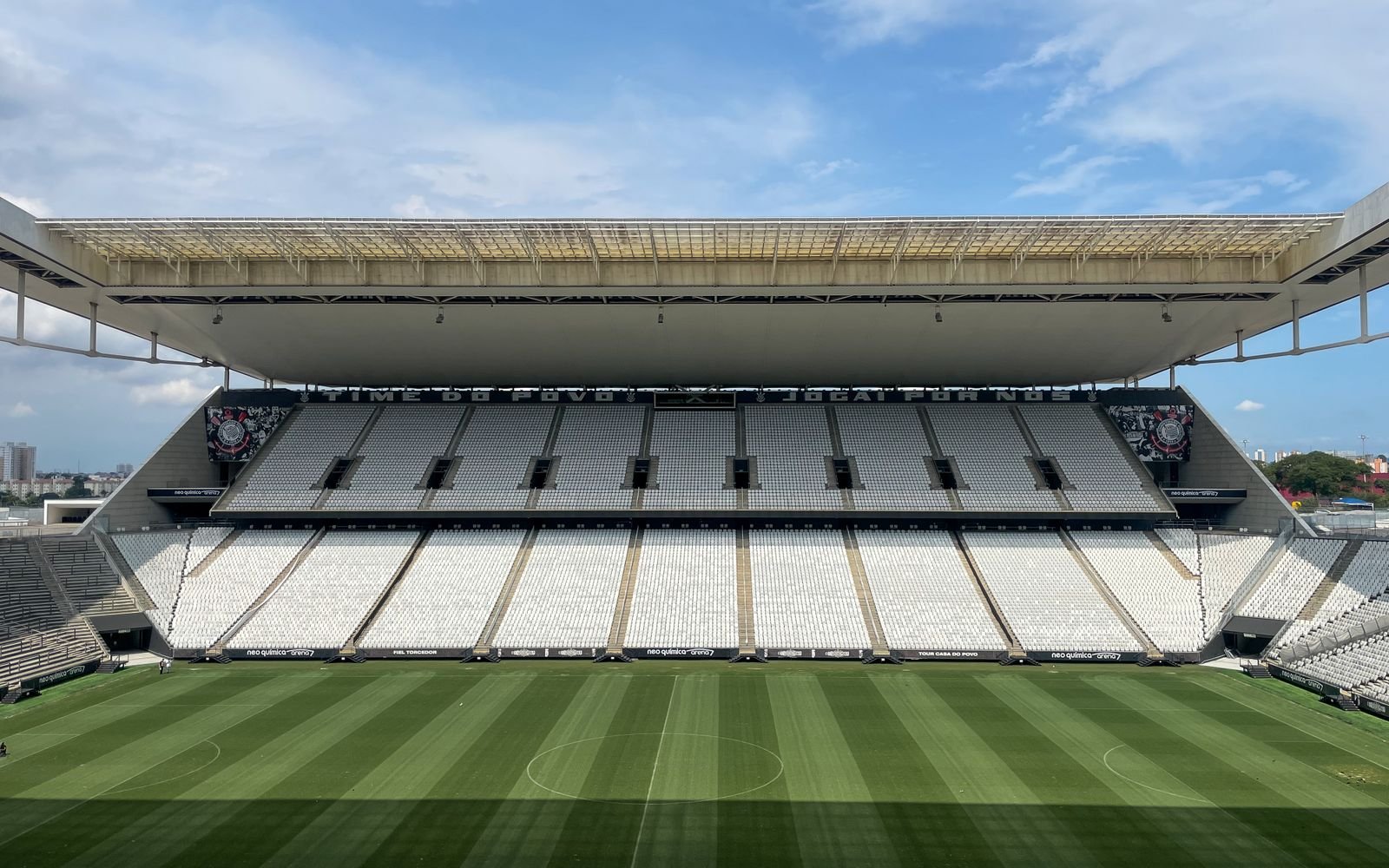 Arquibancada vazia e gramado de estádio de futebol brasileiro, com placas de publicidade ao redor do campo