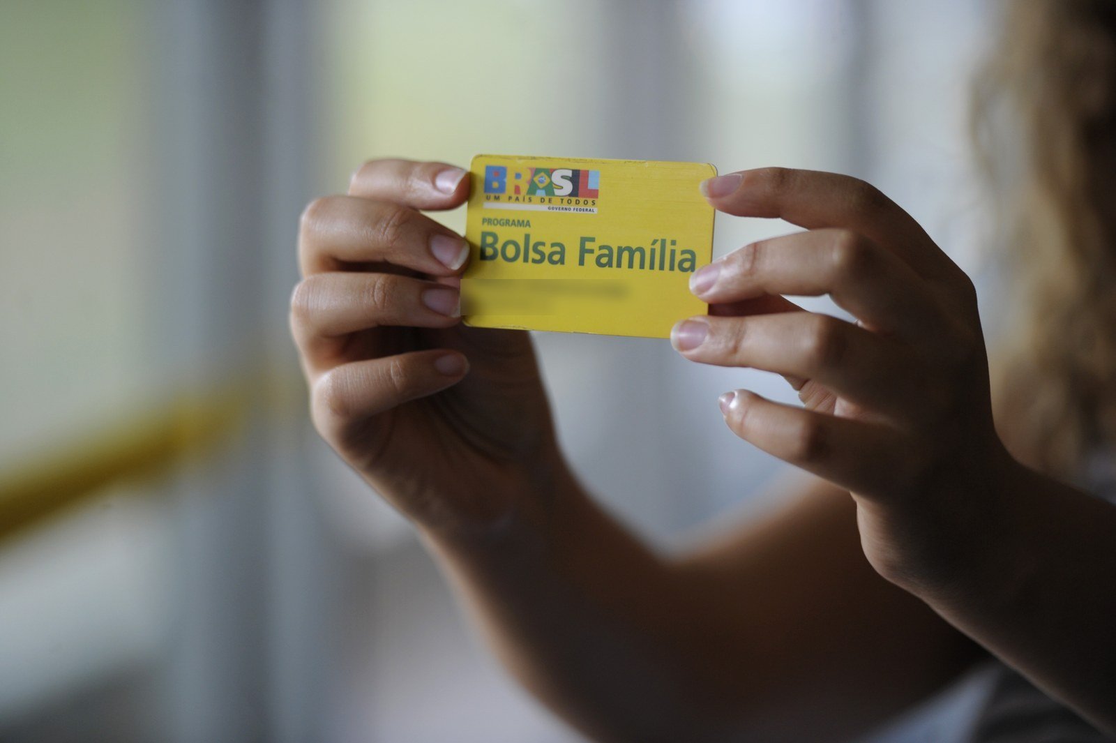 Mãos seguram um cartão amarelo do Programa Bolsa Família, em foto de arquivo; o nome impresso no cartão foi borrado