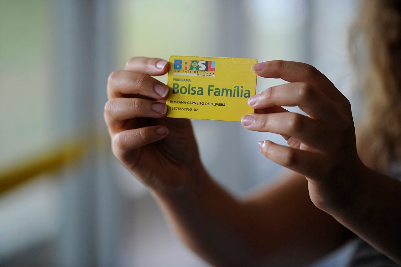 Mãos segurando o cartão amarelo do programa Bolsa Família