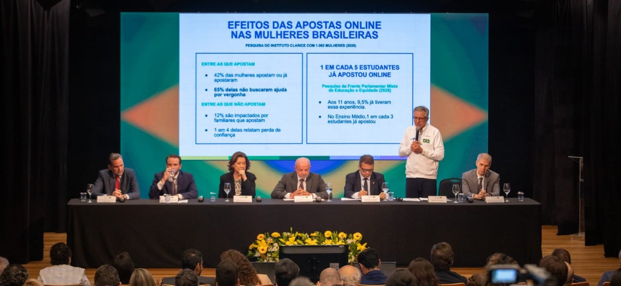 Mesa de autoridades em auditório com telão que exibe dados sobre os efeitos das apostas on-line nas mulheres brasileiras