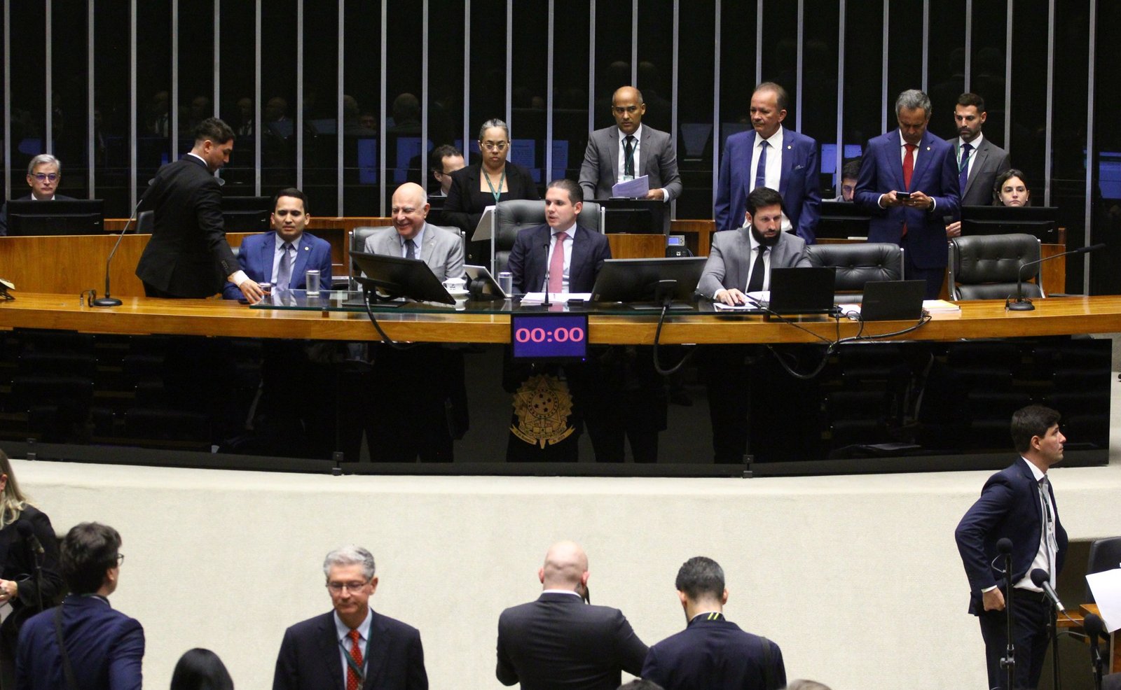 Mesa diretora do Plenário da Câmara dos Deputados durante sessão, com deputados e servidores ao redor