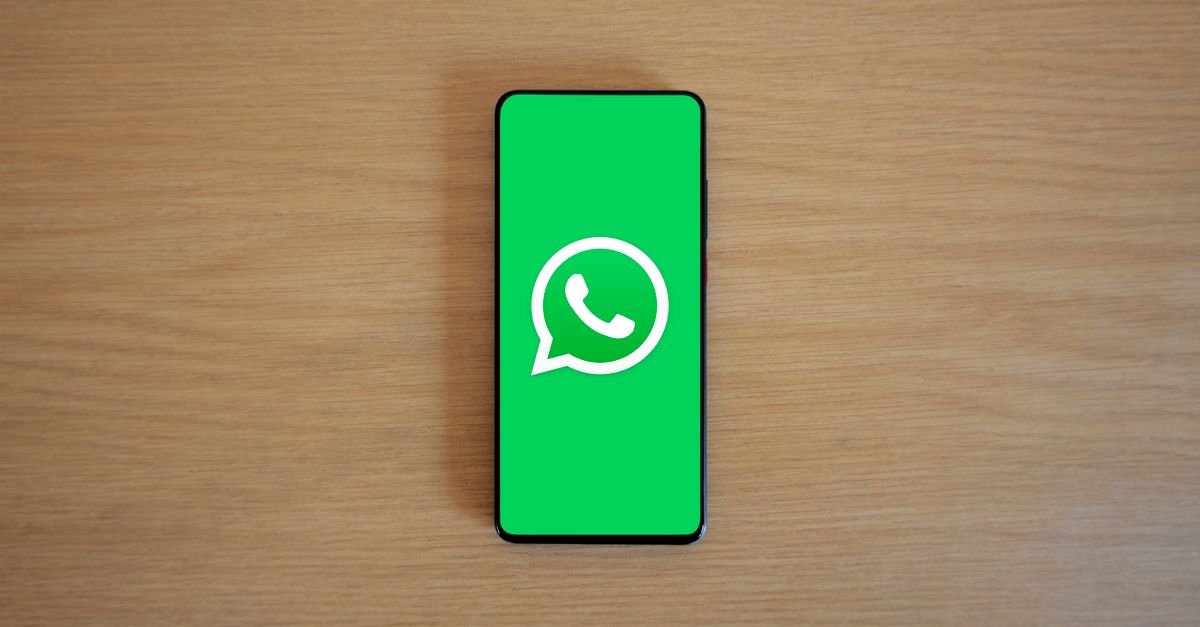 Celular com o logotipo do WhatsApp na tela sobre mesa de madeira