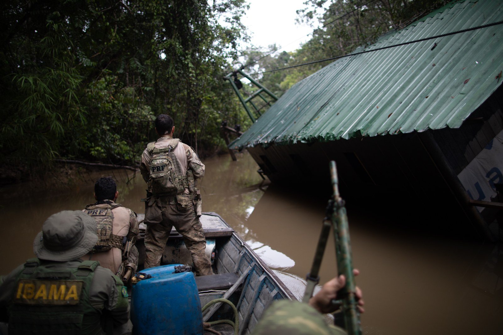 Agentes do Ibama e da PRF em um barco, em operação de fiscalização num rio de mata fechada, diante de uma balsa inclinada