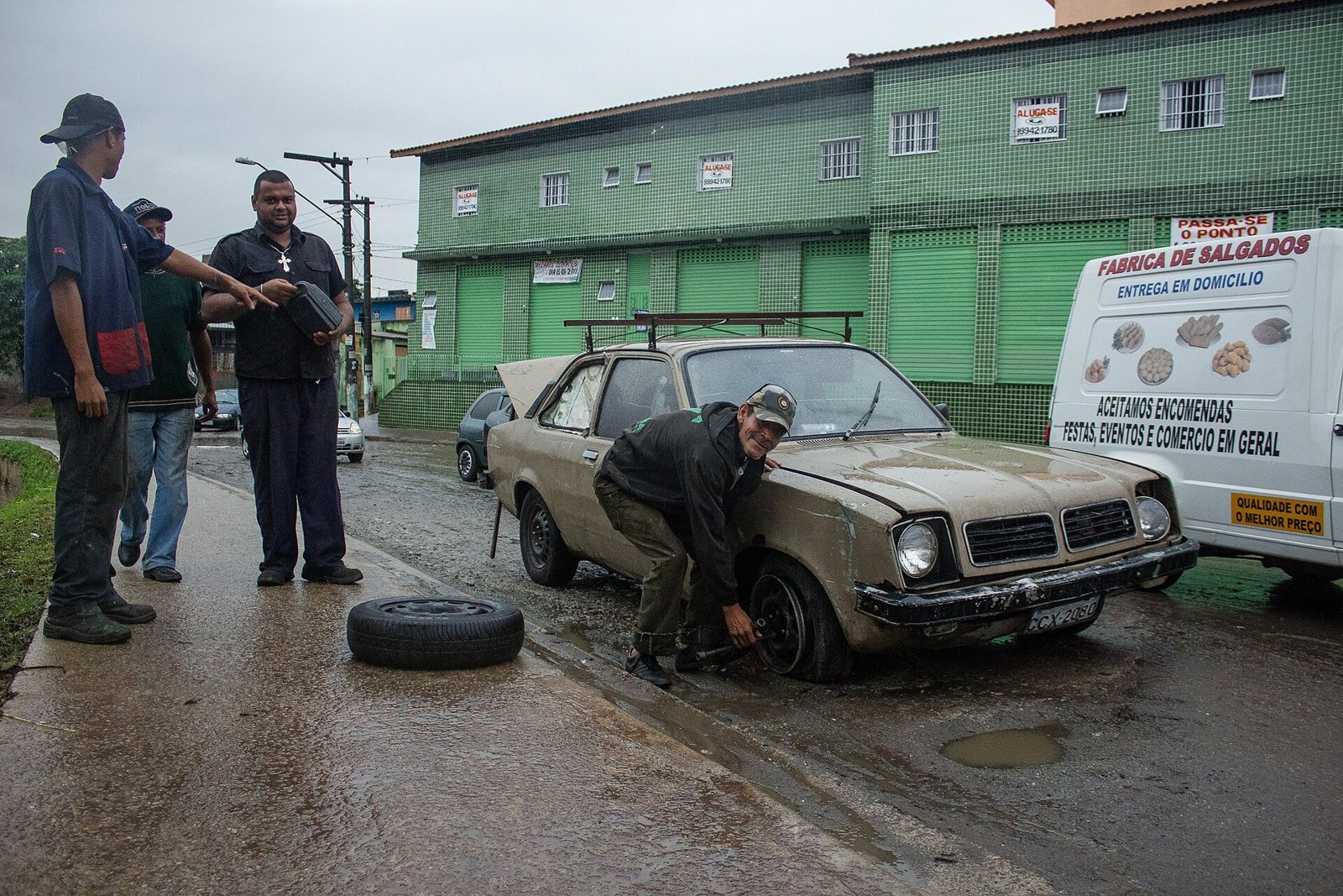 Moradores trocam pneu de carro em rua alagada após chuva forte na Grande São Paulo