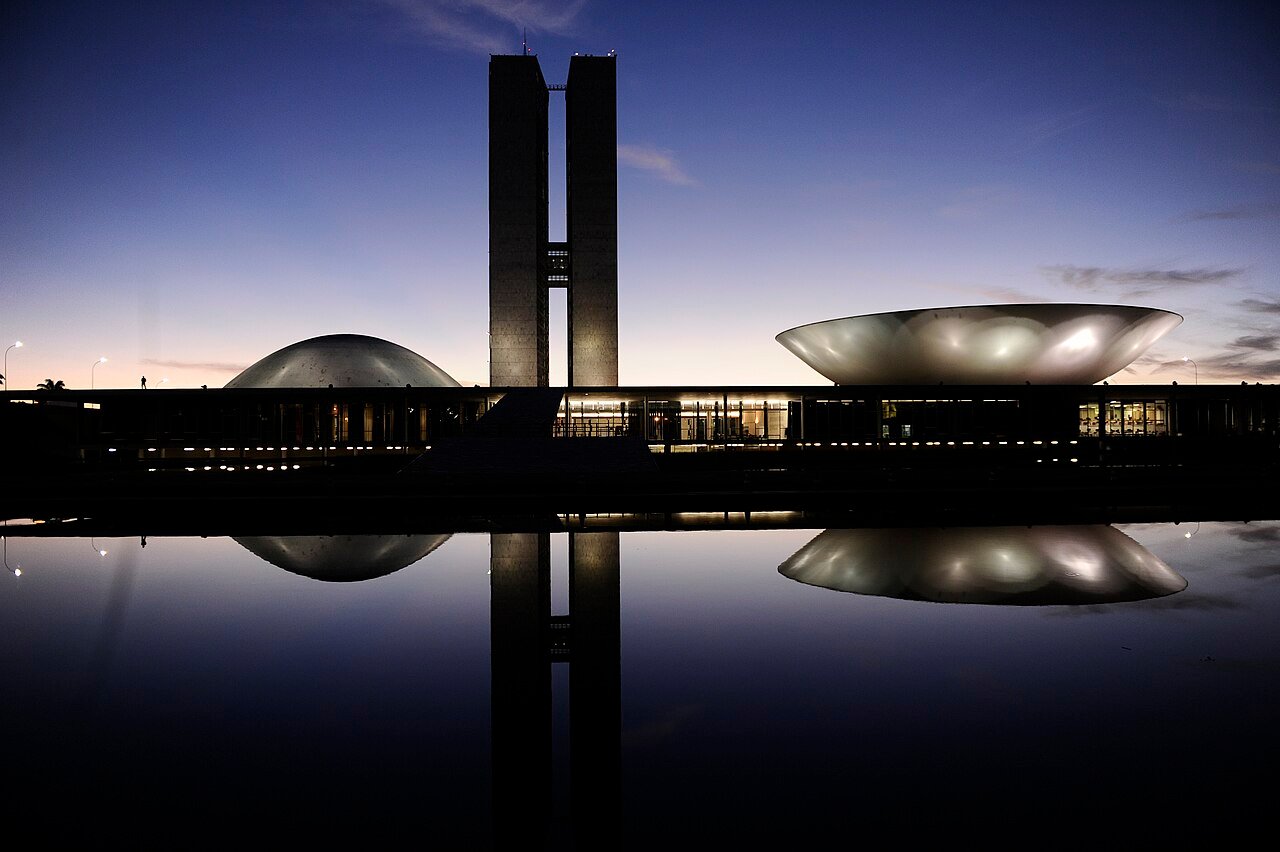 Edifício do Congresso Nacional em Brasília ao entardecer, com as duas cúpulas e as torres refletidas no espelho d'água