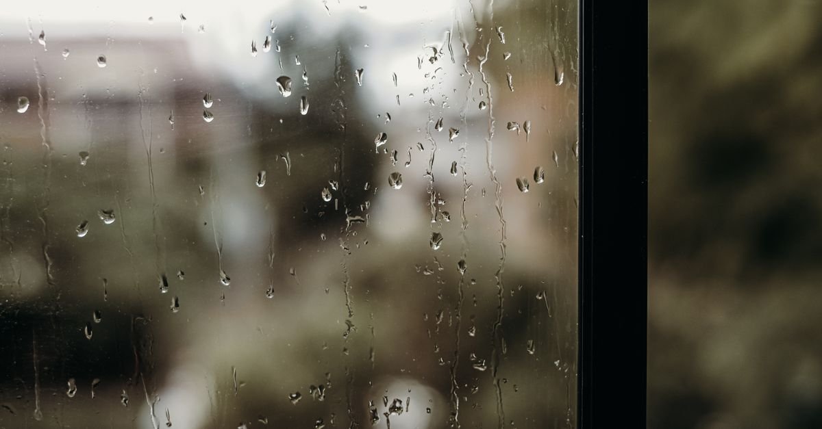 Gotas de chuva escorrendo pelo vidro de uma janela com fundo desfocado