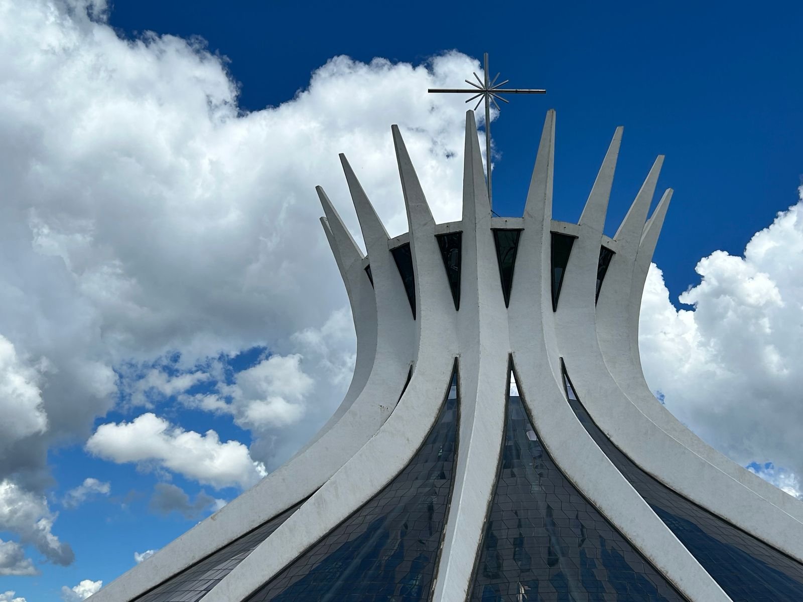 Topo da Catedral de Brasília, com a cruz sobre as colunas de concreto e céu azul com nuvens