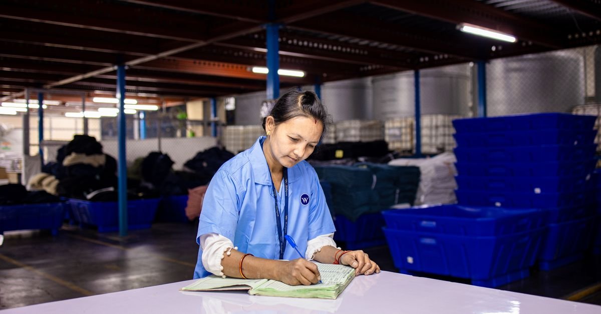 Funcionária de uniforme azul faz anotações em um galpão industrial