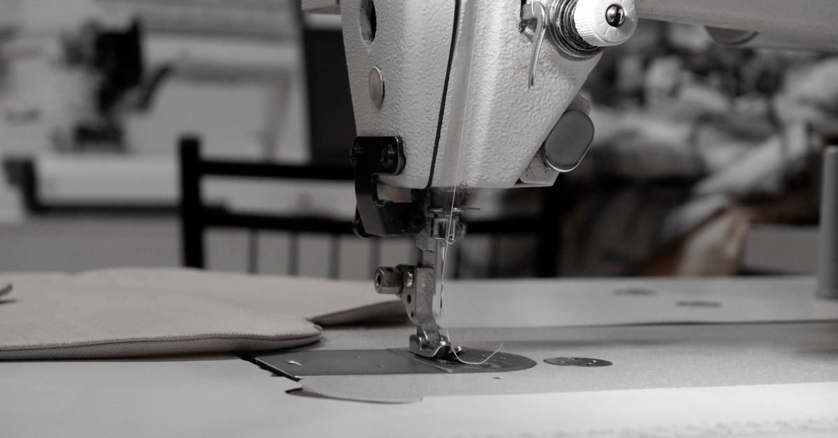Close de máquina de costura industrial com agulha sobre tecido claro em fábrica de confecção