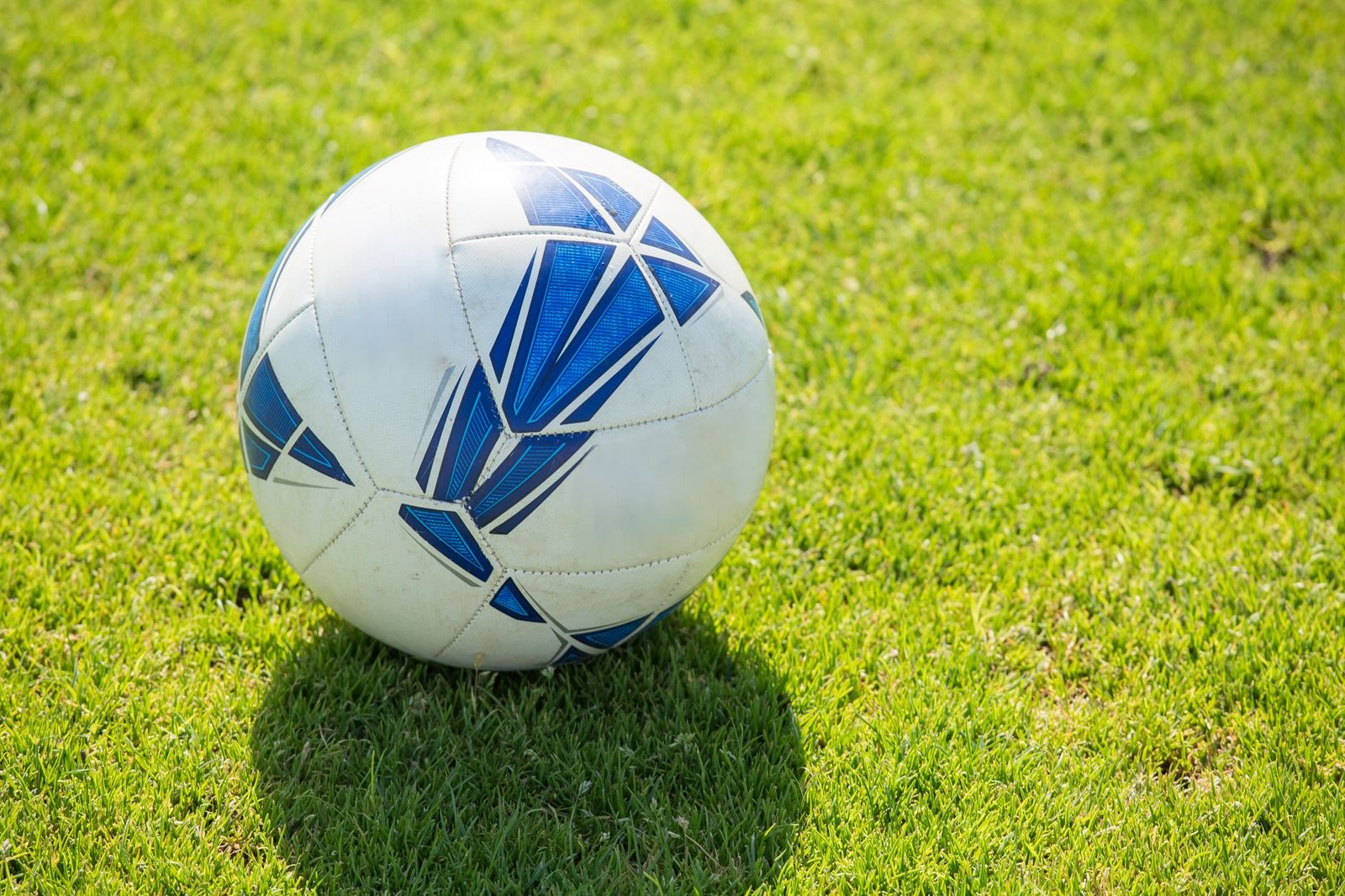 Bola de futebol branca e azul sobre gramado, em primeiro plano