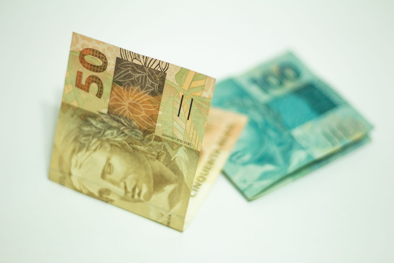 Cédulas de 50 e 100 reais sobre fundo branco, em foto de perto