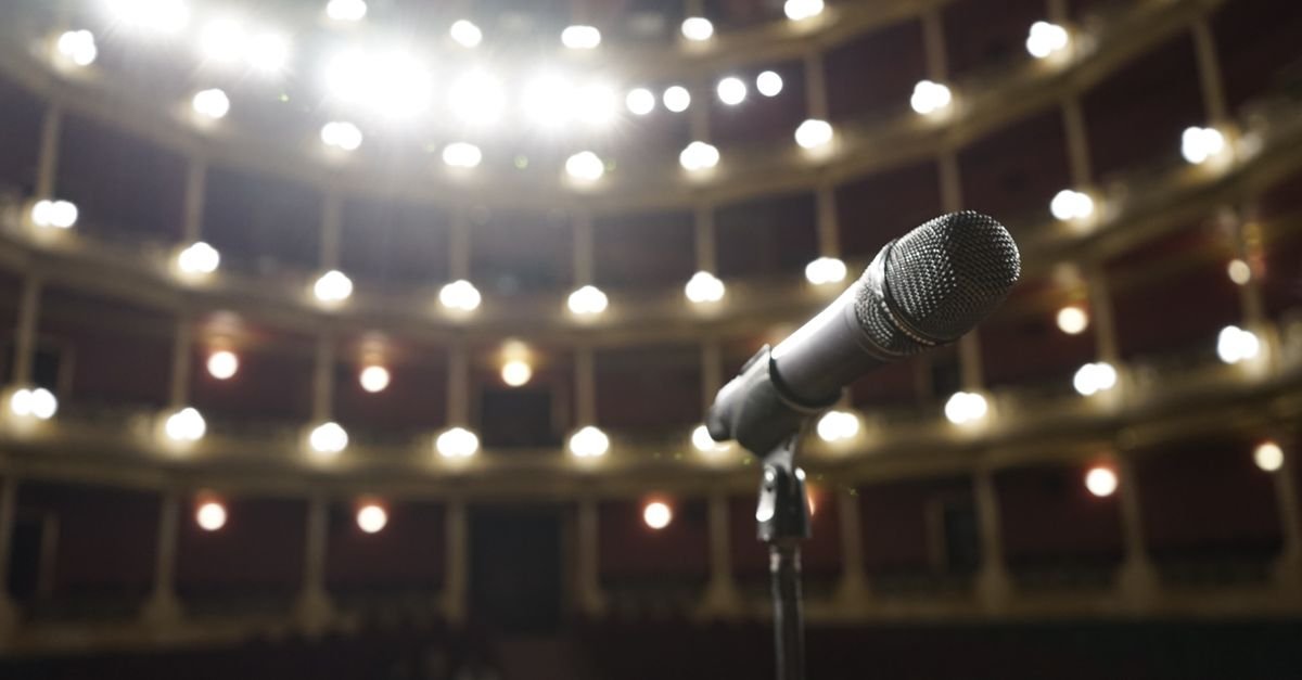 Microfone em pedestal diante de plateia iluminada em auditório