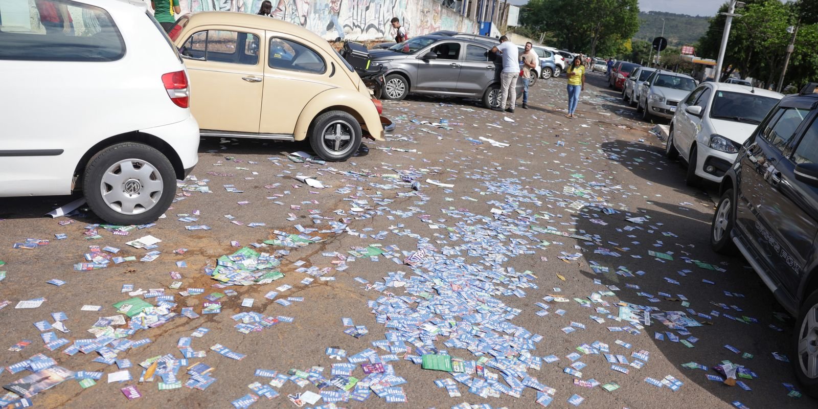 Santinhos espalhados no asfalto perto de carros estacionados na rua de um local de votação, no primeiro turno