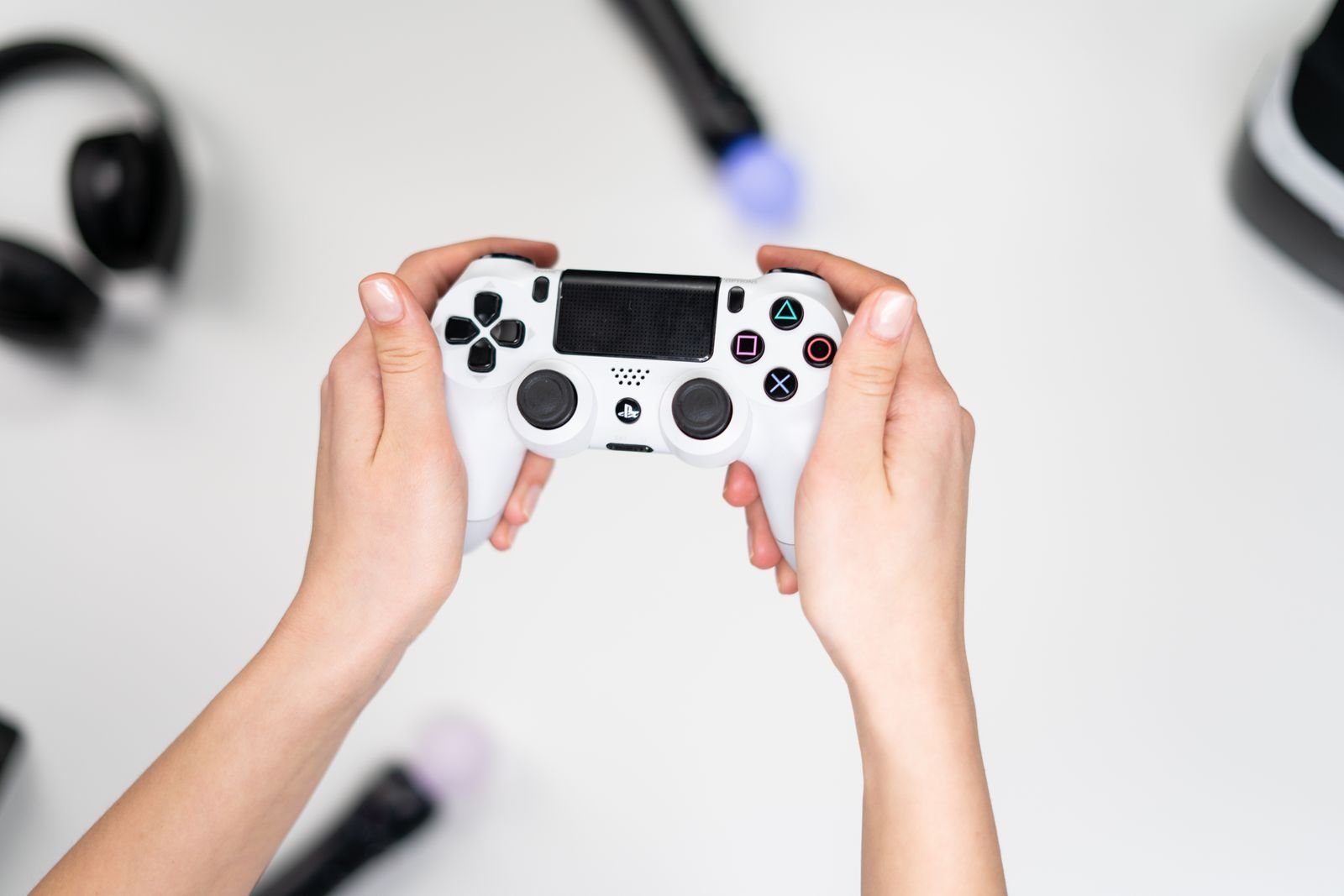 Mãos seguram um controle de videogame branco sobre mesa clara (foto ilustrativa)