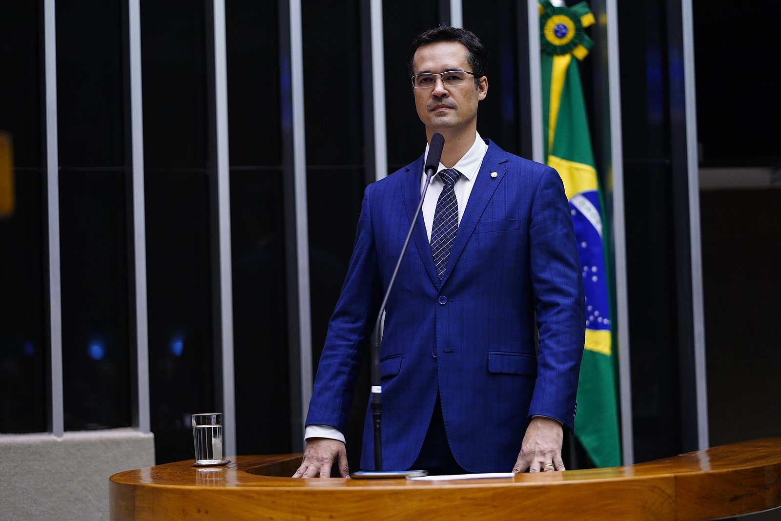 Deltan Dallagnol de terno azul na tribuna do plenário da Câmara dos Deputados, com a bandeira do Brasil ao fundo