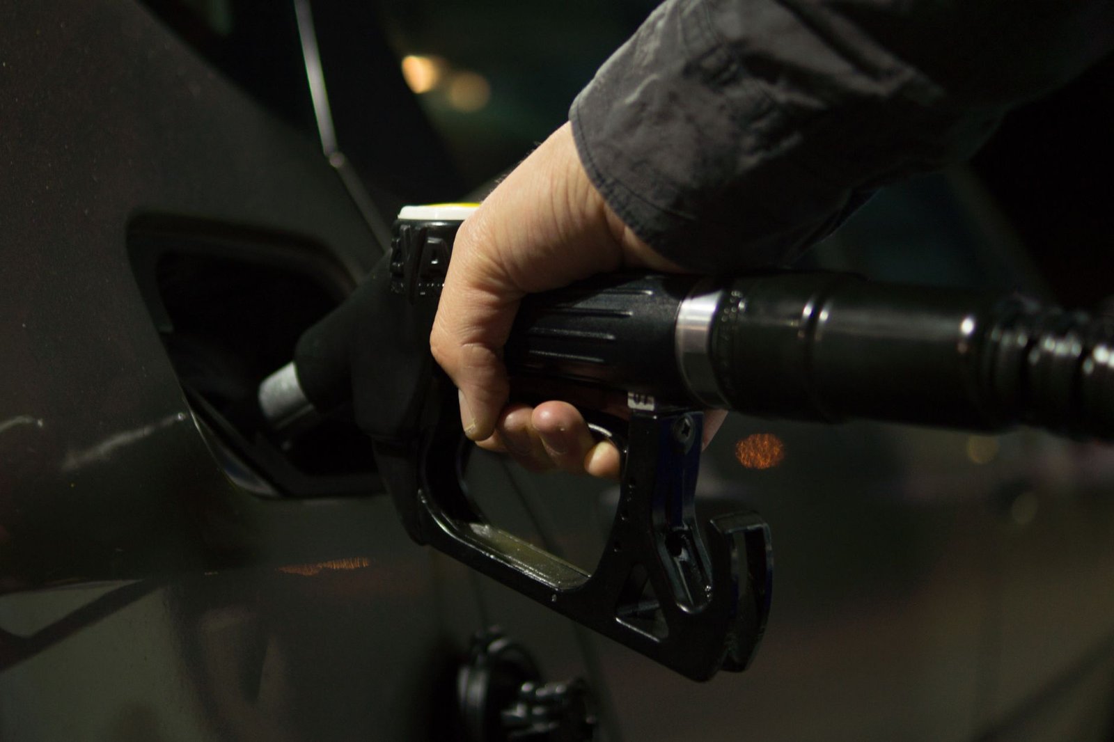 Mão segura bico de abastecimento preto no tanque de um carro, à noite, em posto de combustível (foto ilustrativa)