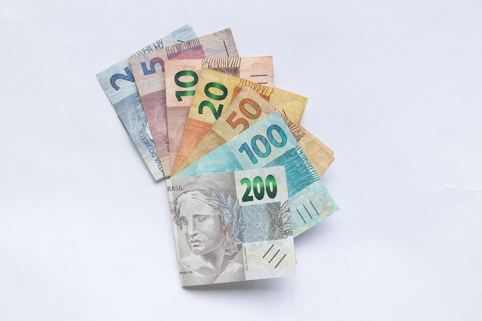 Cédulas de real de 2, 5, 10, 20, 50, 100 e 200 dispostas em leque sobre fundo branco