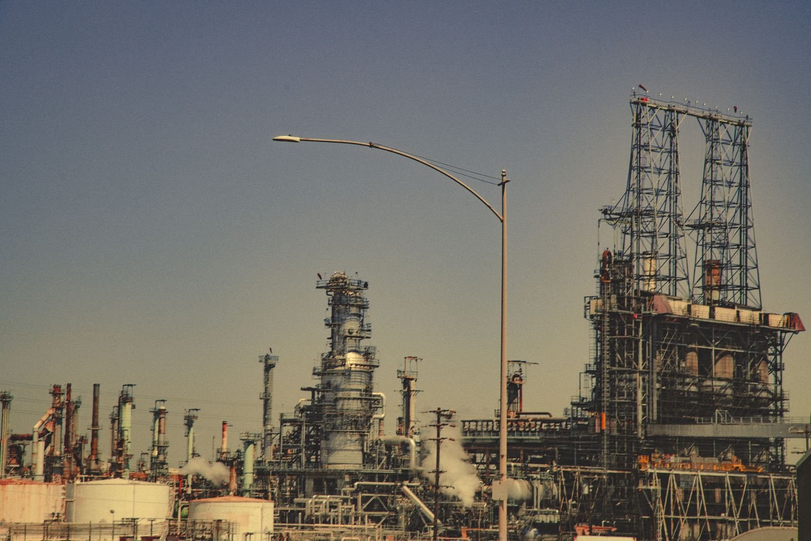 Torres e tubulações de uma refinaria de petróleo sob céu azul-acinzentado