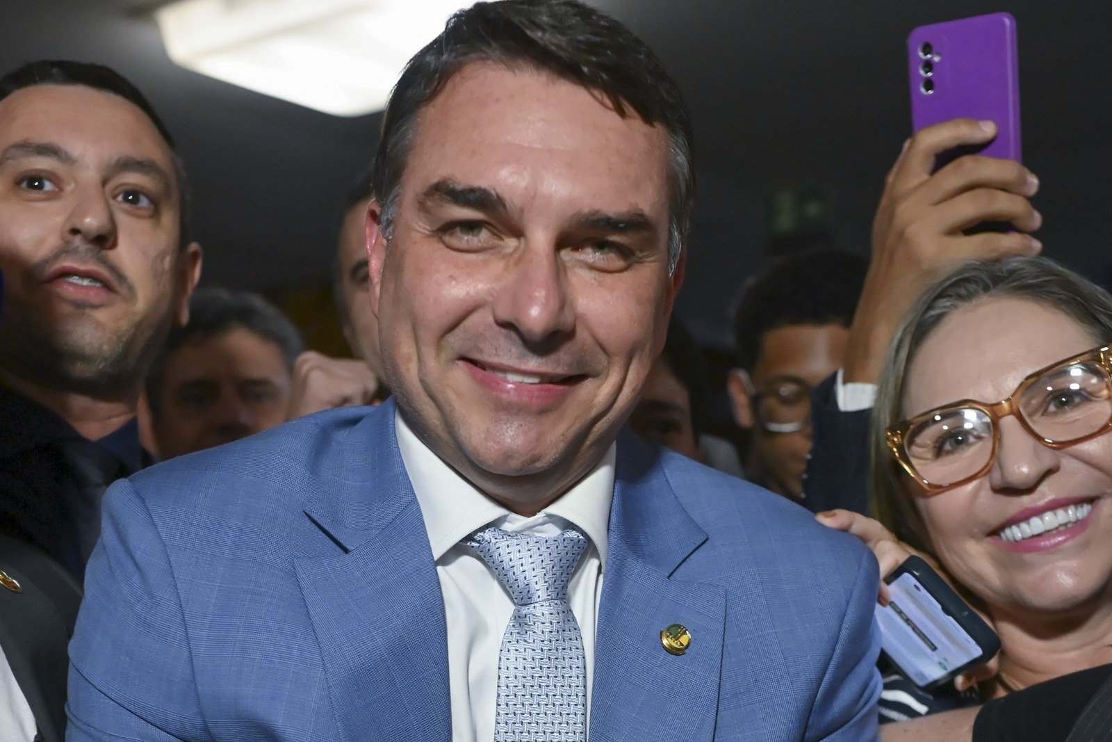 O senador Flávio Bolsonaro sorri durante entrevista no Senado, de terno azul, cercado por apoiadores (foto de arquivo, abril de 2026)