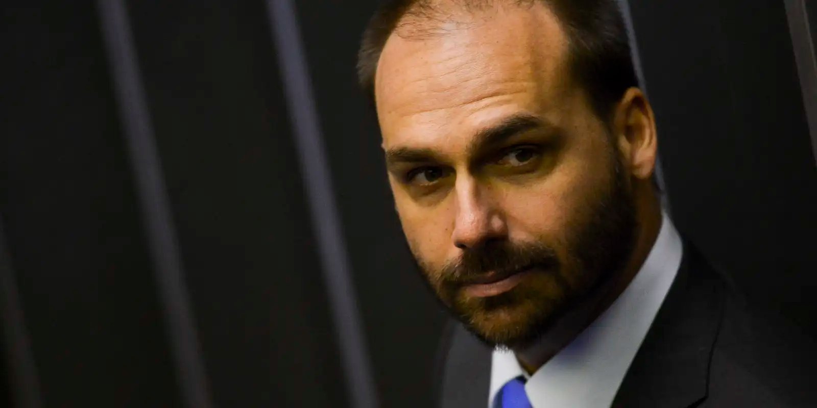 Eduardo Bolsonaro de terno, em plano fechado, olha para o lado