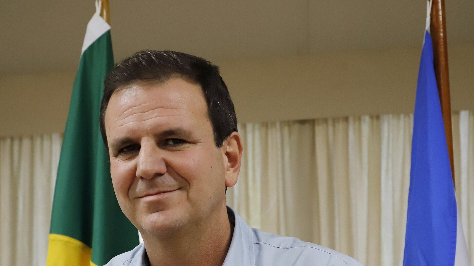 Retrato do prefeito Eduardo Paes diante das bandeiras do Brasil e do Rio de Janeiro