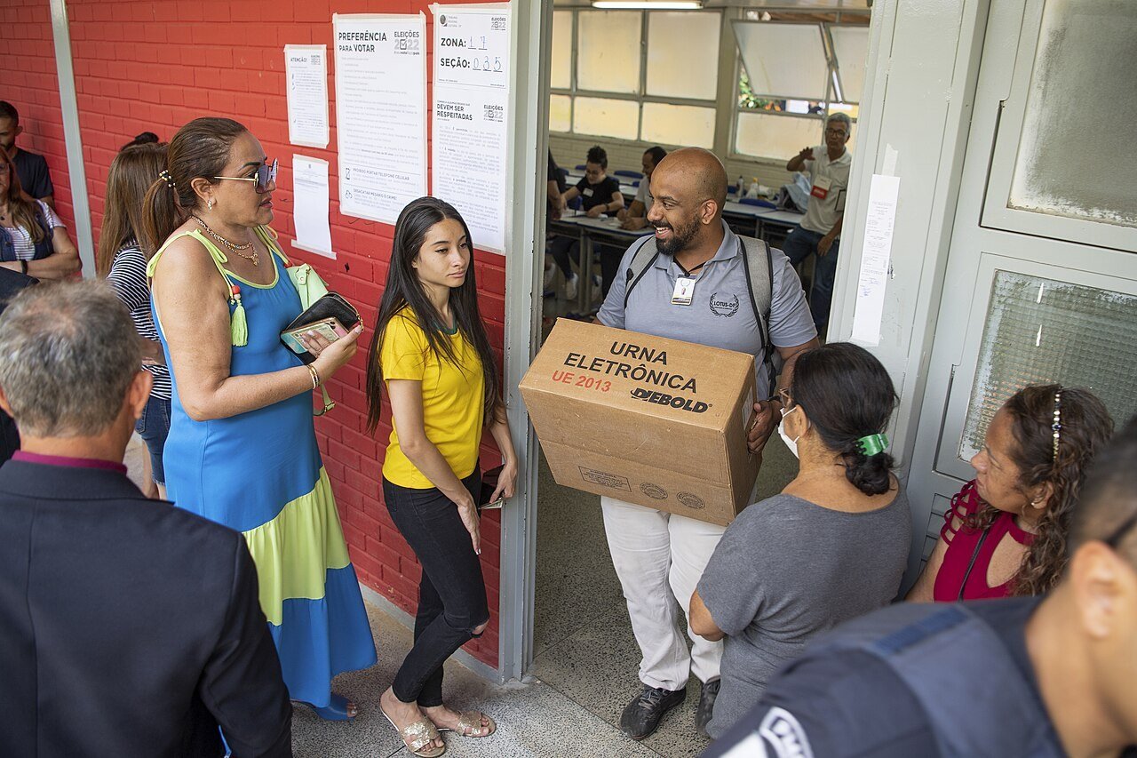 Mesário carrega caixa com urna eletrônica diante de eleitores na porta de uma seção, no segundo turno de 2022 (foto de arquivo)