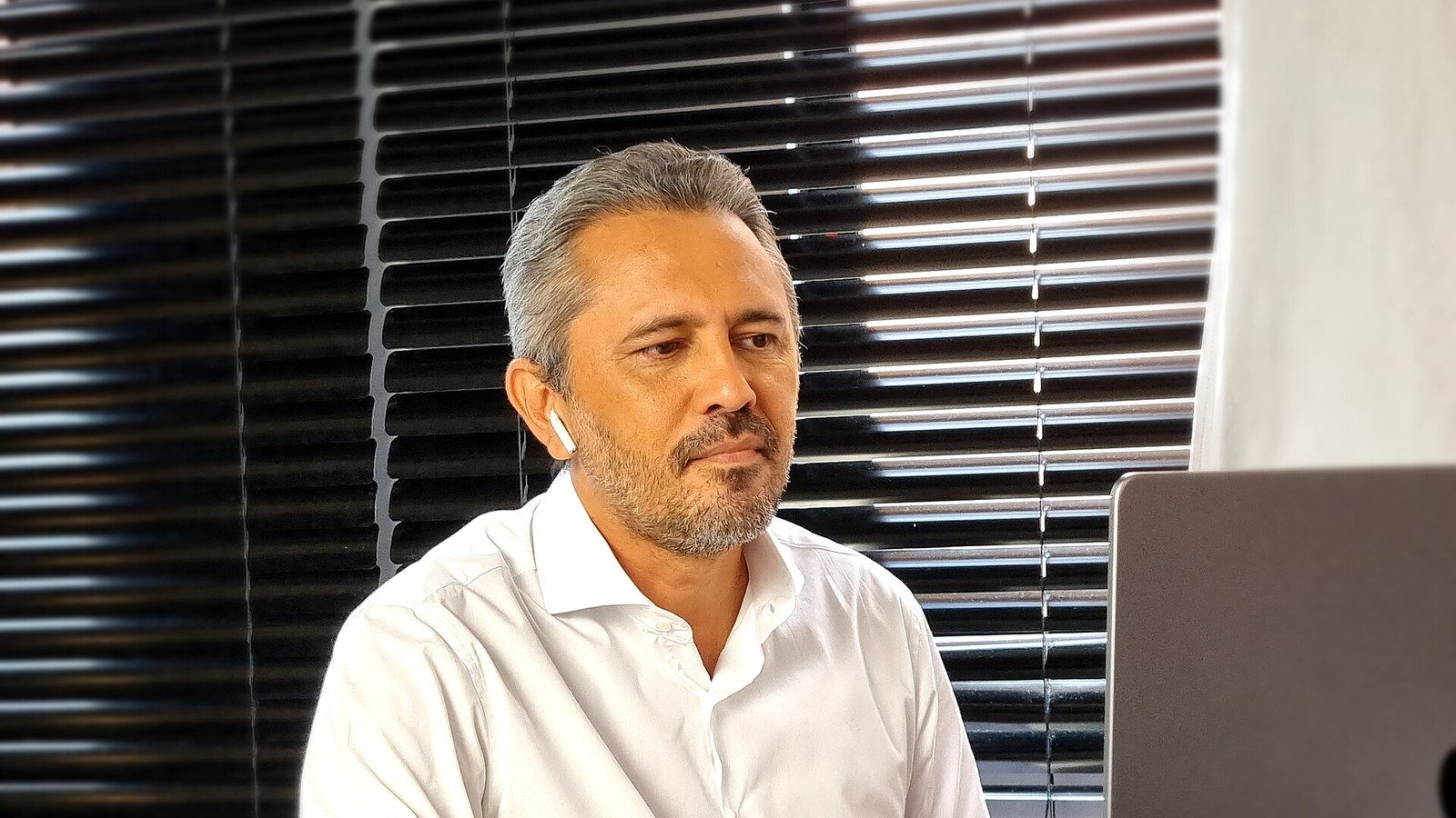 Elmano de Freitas diante de um notebook, com persianas ao fundo