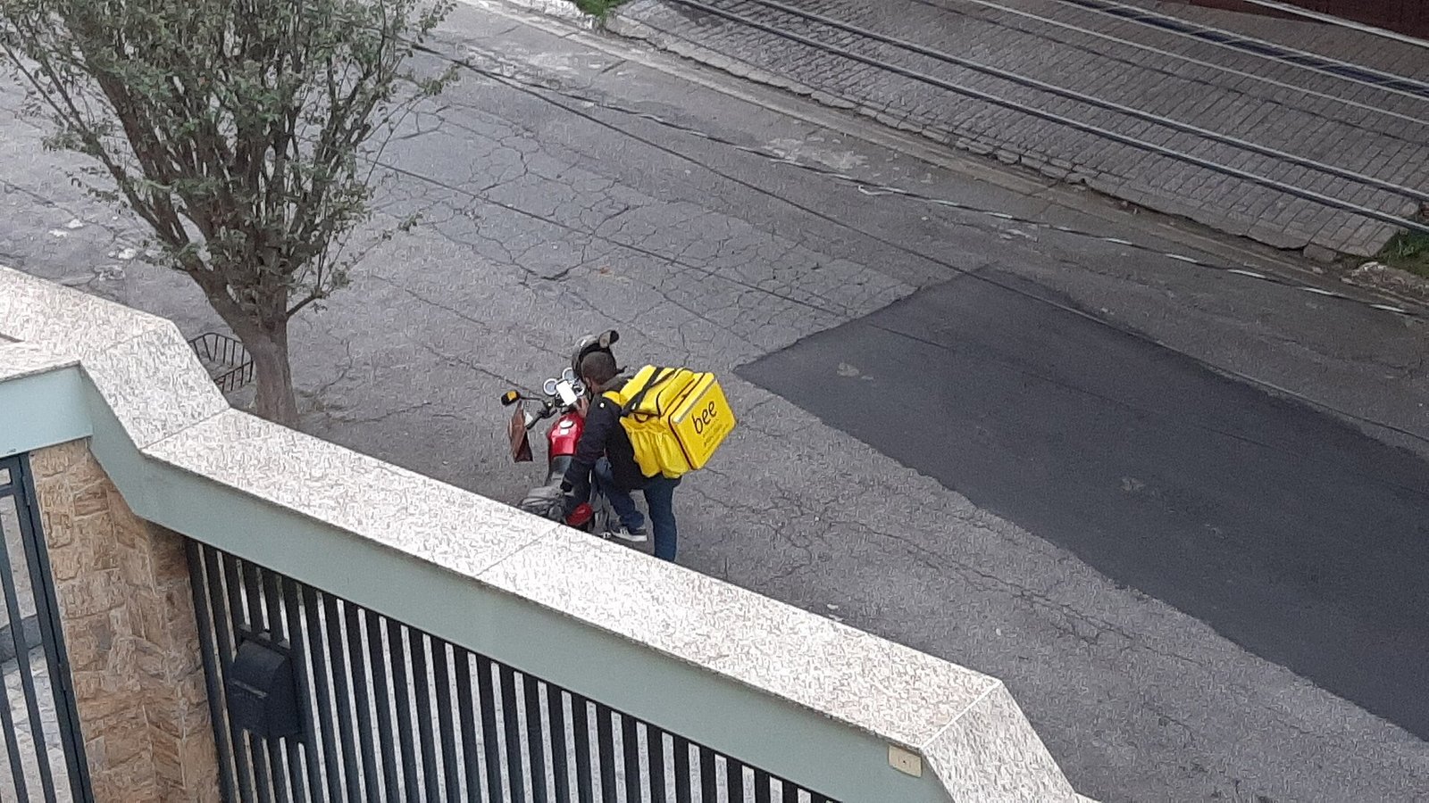 Entregador com bag térmica amarela ao lado de motocicleta em rua residencial