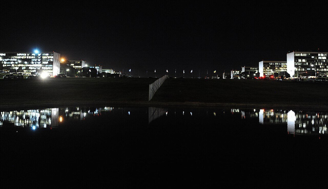 Prédios dos ministérios na Esplanada, em Brasília, iluminados à noite, com reflexo no espelho d'água