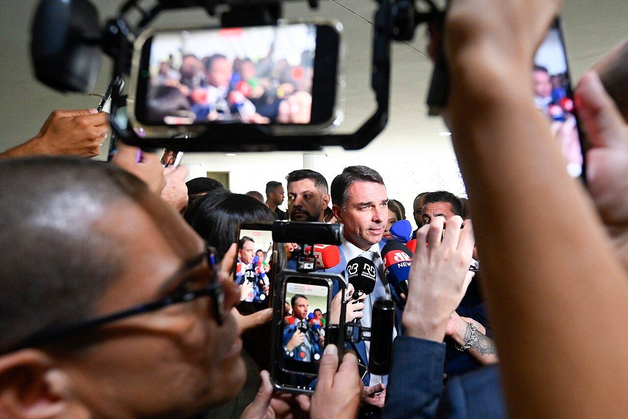 Senador Flávio Bolsonaro cercado por microfones e câmeras durante entrevista