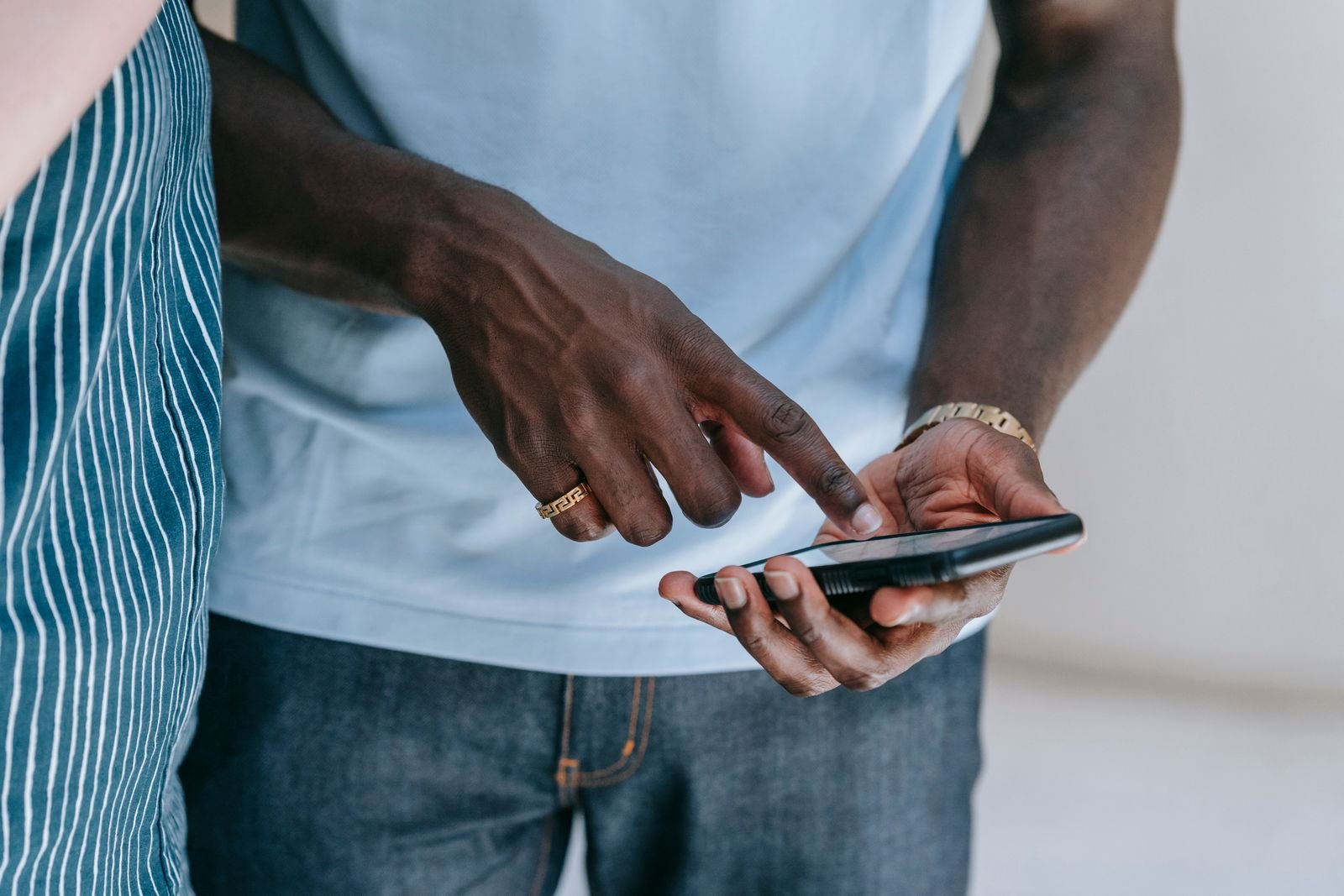 Mãos seguram um celular enquanto outra pessoa aponta para a tela (foto ilustrativa)