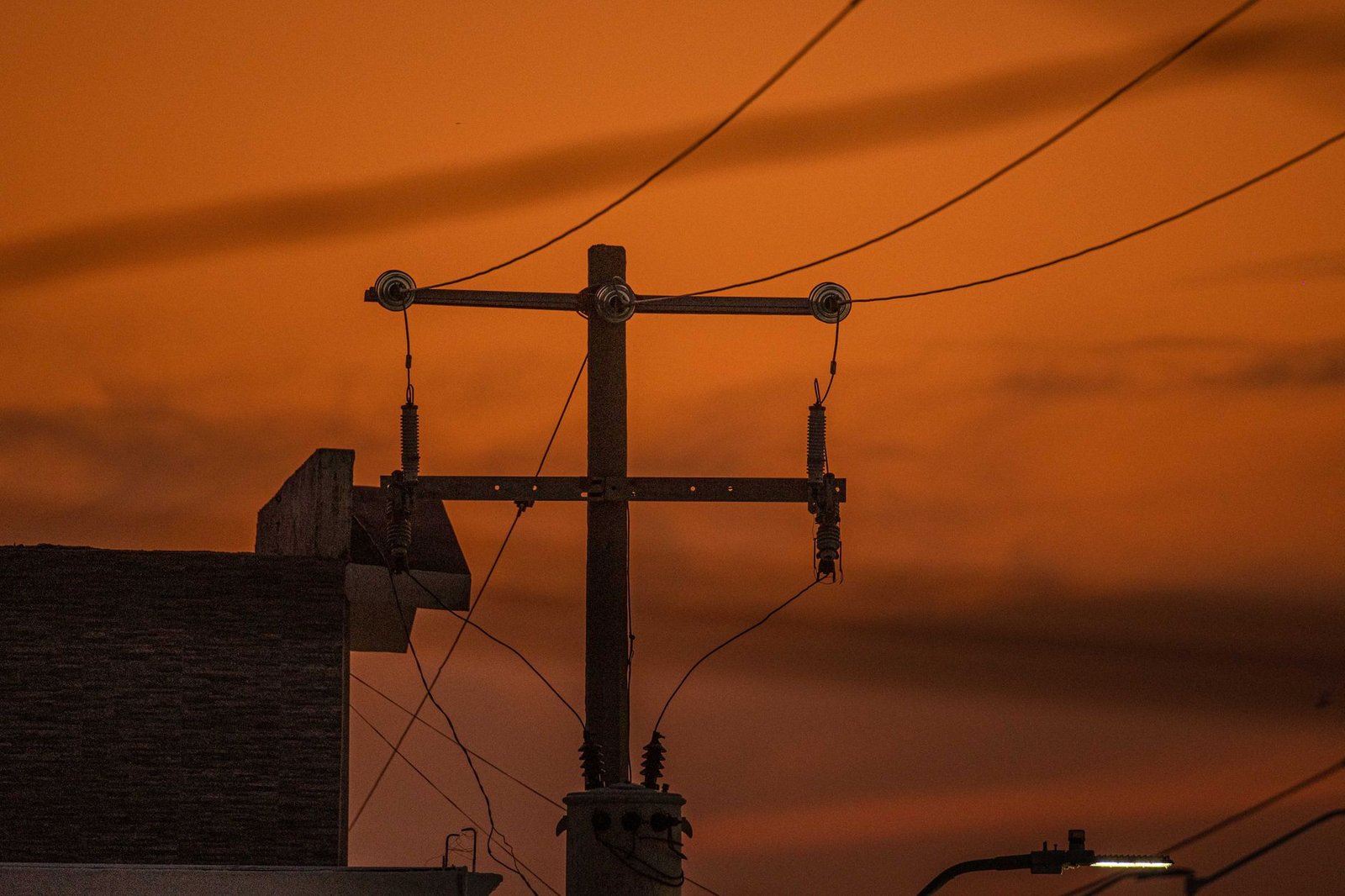 Poste de distribuição de energia elétrica e fios em silhueta contra o céu laranja do entardecer