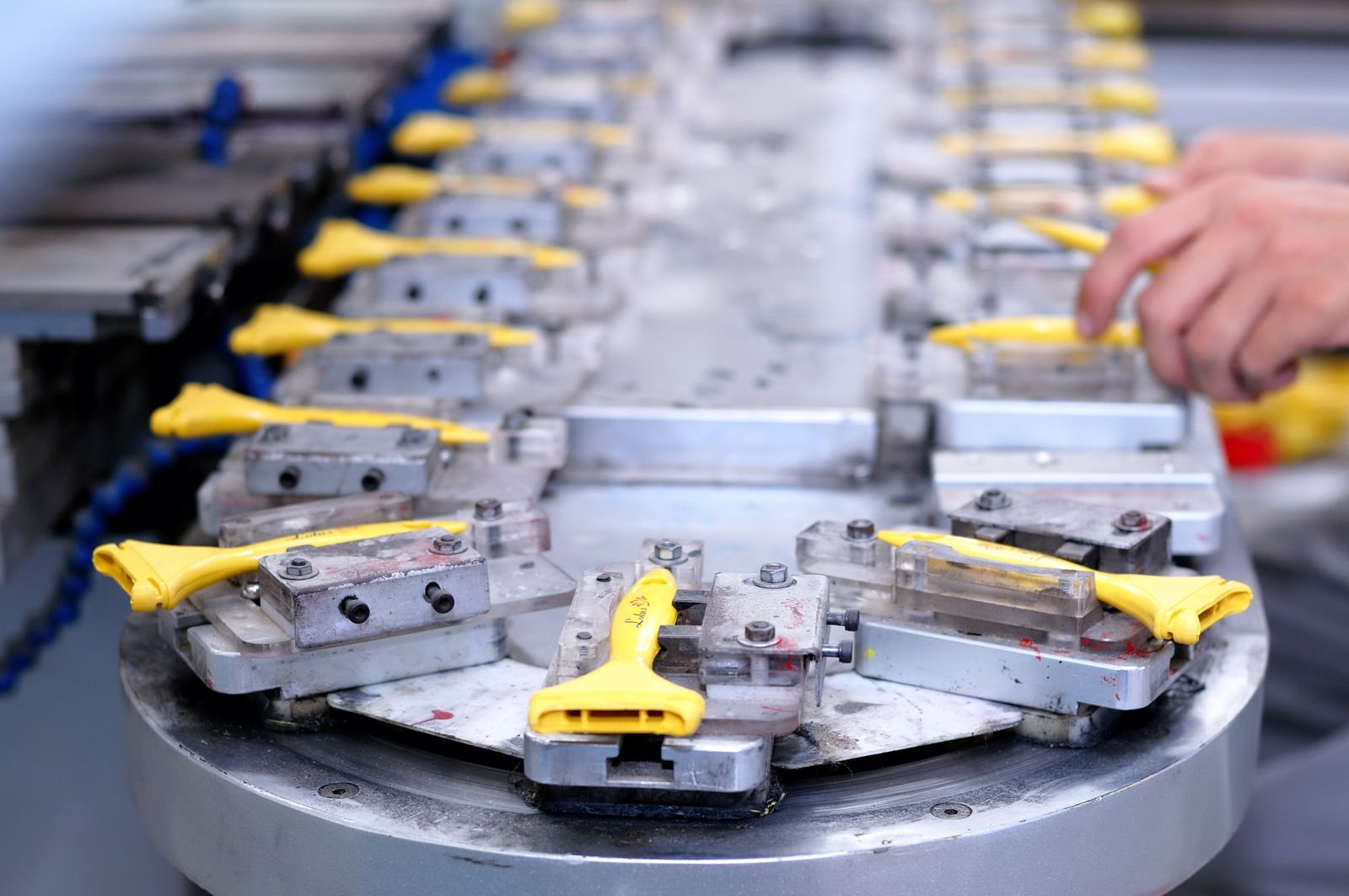 Peças amarelas presas em uma linha de produção industrial, com mãos de um operário ao fundo
