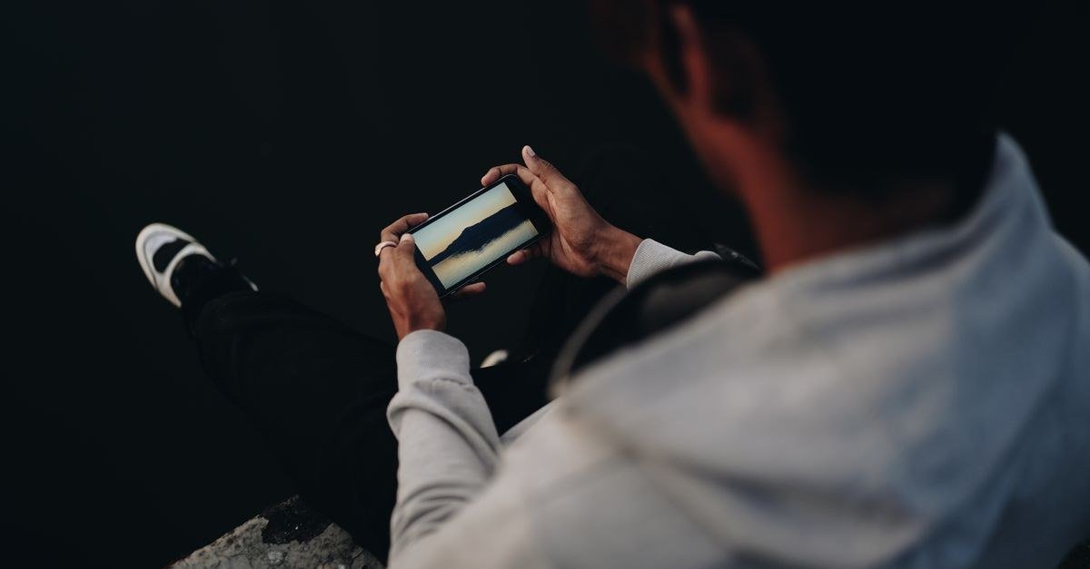Pessoa sentada assiste a um vídeo no celular segurado na horizontal, em ambiente escuro