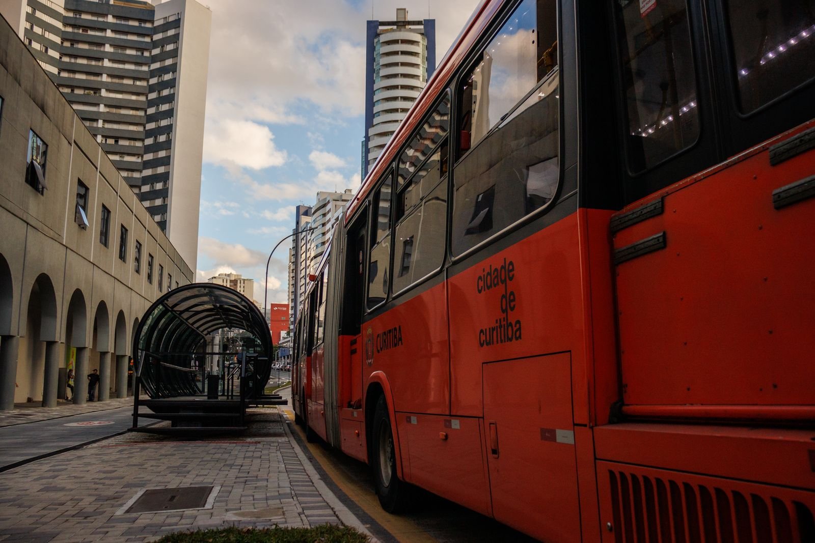 Ônibus articulado vermelho parado em ponto de embarque em Curitiba (foto ilustrativa)