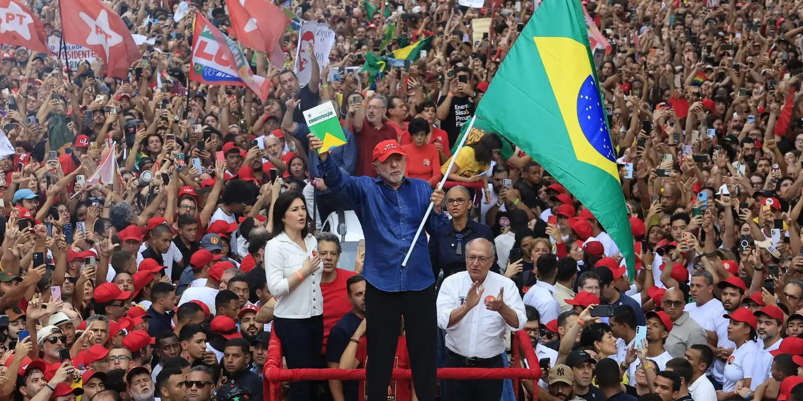 Lula ergue um exemplar da Constituição ao lado de Alckmin e Simone Tebet diante de multidão na Avenida Paulista, em São Paulo