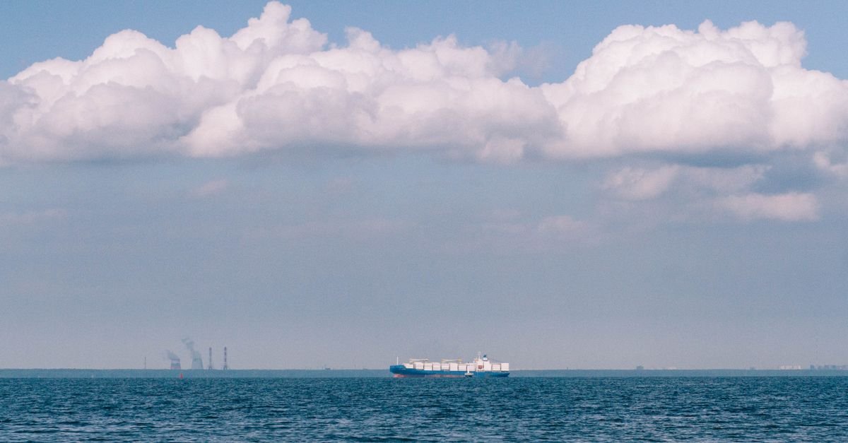 Navio cargueiro navegando ao longe em mar aberto sob céu com nuvens densas