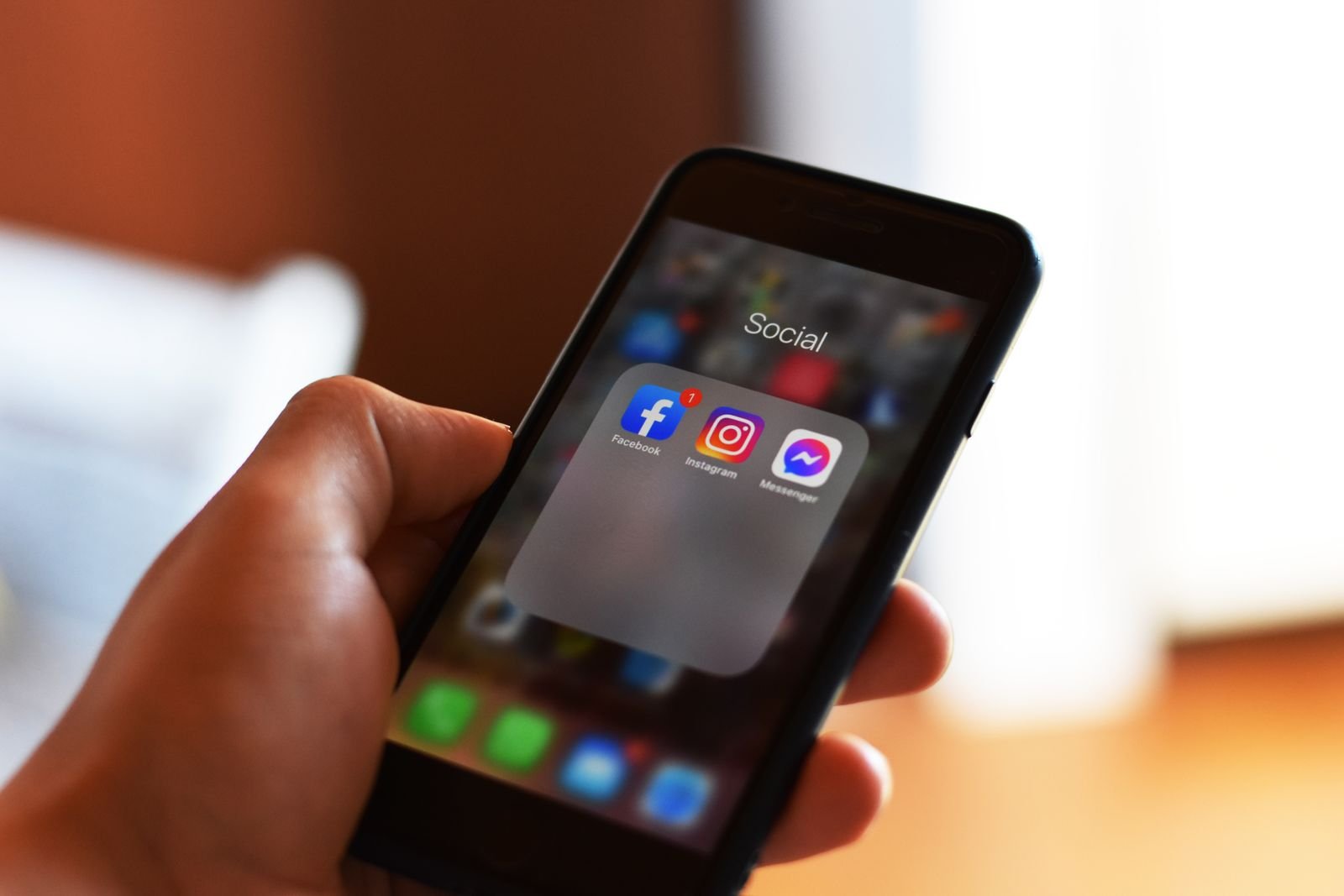 Mão segura um celular com os ícones do Facebook, Instagram e Messenger em uma pasta de aplicativos