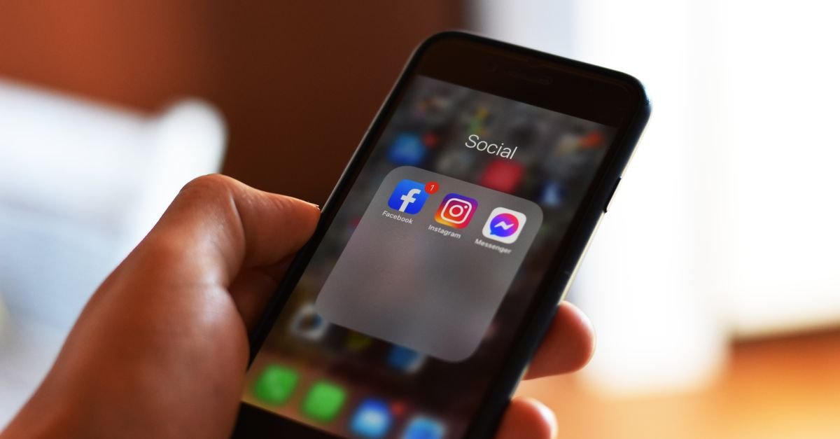 Mão segura smartphone com ícones de Facebook, Instagram e Messenger na tela