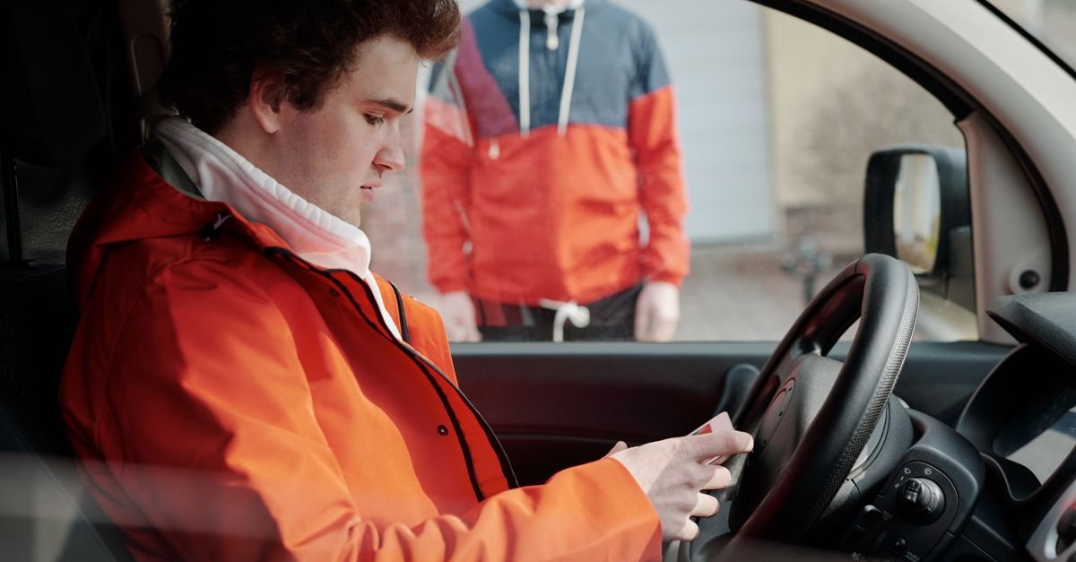 Motorista sentado ao volante de um carro, com o celular na mão, em foto de arquivo